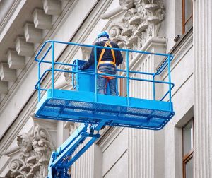 a man on a blue lift working on a building.