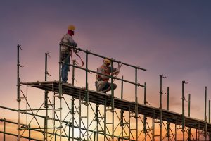 Two men atop metal construction scaffolding.